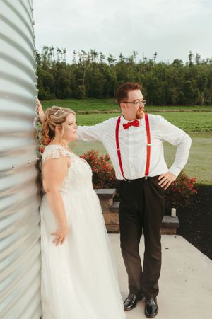 Couple pose together against a metal silo wall with green fields in the background.