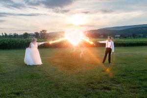 Dramatic sunburst between newlyweds in an open field during golden hour.