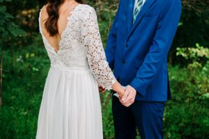 Close-up of wedding dress details showing lace sleeves and back with couple holding hands.
