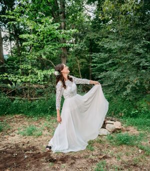 Bride in lace sleeve wedding gown twirling in a forest clearing.