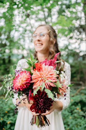 Beautiful bouquet of coral and burgundy dahlias with greenery held in outdoor setting.