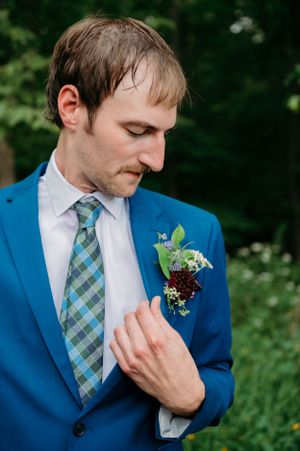 A groom in a bright blue suit adjusts his plaid tie while wearing a delicate floral boutonniere.