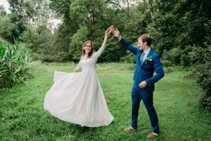 A couple dances playfully on a lush green lawn surrounded by tall grass and trees.