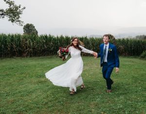 The newlyweds dance joyfully in a field with cornfields in the background.