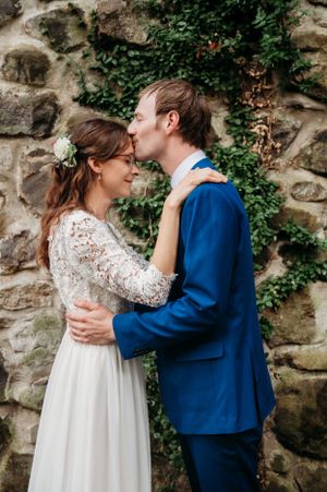 An intimate moment between newlyweds against a rustic stone wall covered in ivy.