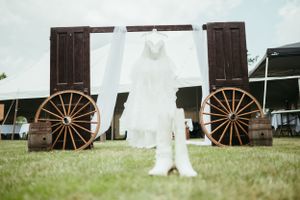 A wedding dress displayed between rustic wooden wagon wheels outdoors.