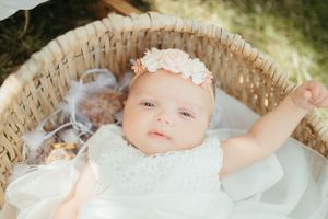 A baby wearing a white floral headband lying in a wicker basket.
