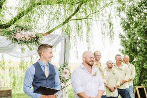 An outdoor wedding ceremony under a willow tree with floral arch decorations.