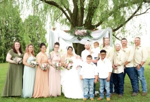 Wedding party poses under a weeping willow tree with bridesmaids in pastel dresses and groomsmen in casual attire.