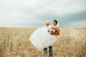 A romantic moment captured in a wheat field as a groom carries his bride in her flowing white dress.