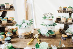 Rustic wedding dessert display featuring cupcakes and cake on wooden stands with greenery accents.