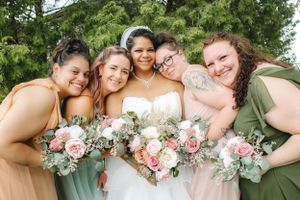 Bridesmaids in pastel dresses share joyful smiles while holding pink and white bouquets.