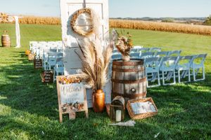 Rustic wedding decor with wooden barrels, pampas grass, and welcome signs against a rural farm backdrop.