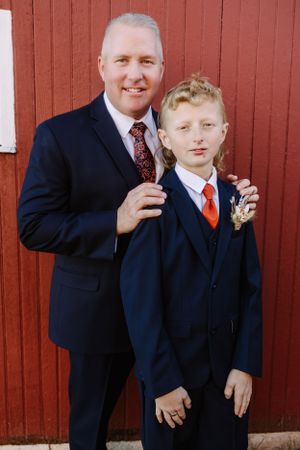 Portrait in front of a red barn featuring matching navy suits and orange ties.