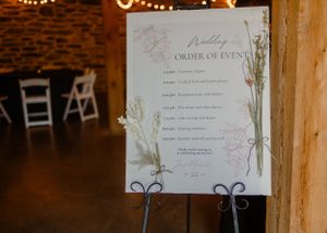 An elegant wedding timeline sign displayed on an easel with floral design elements.