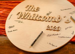 Wooden circular guestbook with 'The Whitcomb 2023' engraved on red textured background.