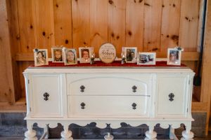 Vintage white dresser decorated with framed photographs on display against rustic wooden paneling.
