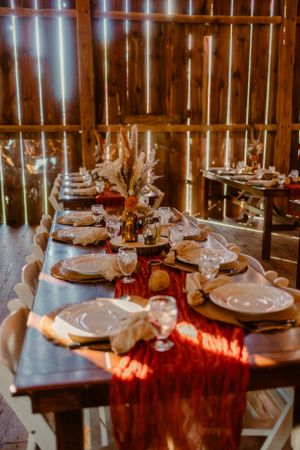 Elegant table setting with burgundy runner and pampas grass centerpieces in rustic barn venue.
