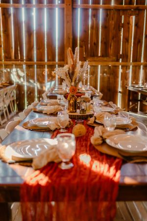 Wedding table setting with red runner and rustic decor in warm barn lighting.