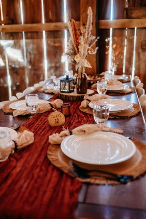 Rustic wedding table setting with burgundy runner, wooden chargers and dried flower centerpiece.