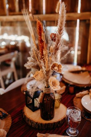 Dried flower arrangement in amber bottle centerpiece on wooden slice charger.