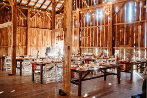 Interior of a rustic barn wedding venue with wooden beams and arranged dining tables.