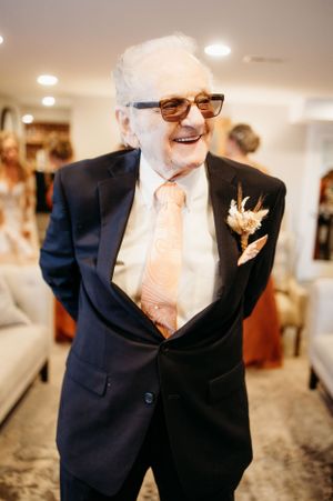 A joyful moment captured of a gentleman in a navy suit and peach tie at a formal event.