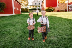 Two young ring bearers in suspenders holding wooden signs on a grassy lawn.