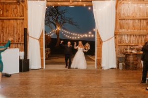 Rustic barn wedding venue with string lights and white curtains framing a wooden dance floor.