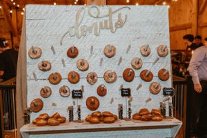 A creative donut wall display with white script lettering at a rustic wedding reception.