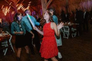 Guests dancing energetically at a barn wedding reception with string lights overhead.
