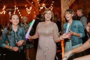 Party guests dance and celebrate at a rustic barn wedding reception with string lights overhead.