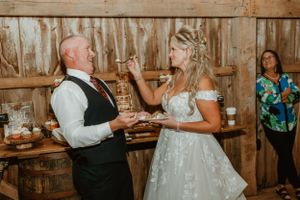 A couple playfully shares wedding cake during their rustic barn reception.