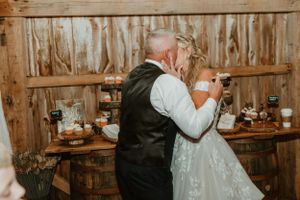 A couple playfully feeds each other wedding cake at their rustic barn reception.