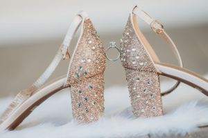 Sparkly rose gold bridal heels with crystal embellishments holding an engagement ring.