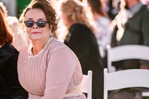 Wedding guest in pink sweater and sunglasses seated at outdoor ceremony.