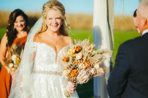 Outdoor fall wedding ceremony with orange floral bouquet and natural scenery.