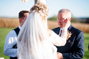 A tender moment during a wedding ceremony on a sunny day with golden fields in the background.