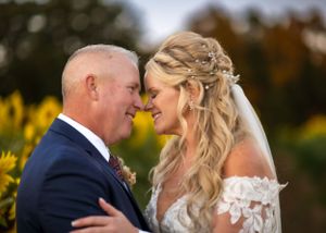 Romantic wedding portrait of a couple embracing in front of blooming yellow sunflowers at sunset.