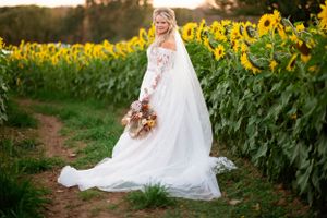 A bride in a lace wedding gown poses elegantly beside a field of tall sunflowers.