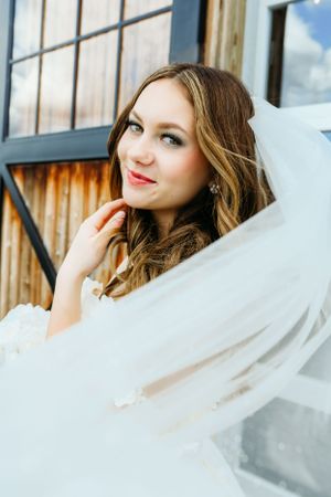 A bride poses outdoors with a flowing white veil and natural makeup.