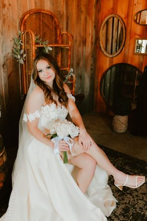 A bride poses in a classic white gown in a rustic room with vintage mirrors and decor.