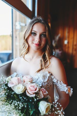 A bride holding a beautiful bouquet of pink roses and baby's breath in soft natural lighting.