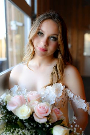 A bride holding a bouquet of pink and white roses in soft window light.