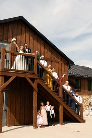 Wedding party members posed on rustic wooden stairs outside a barn venue.