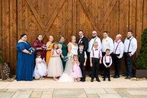 Wedding party in coordinated blue, pink and white attire posed against wooden barn backdrop.