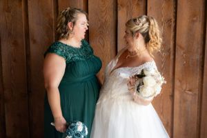 Bridesmaid in emerald green and bride in white share a joyful moment.