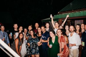 A lively nighttime party scene with a group of people celebrating outdoors near a green-roofed building.