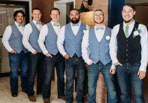 Groomsmen lined up wearing matching grey vests and dress shirts against a brick wall.