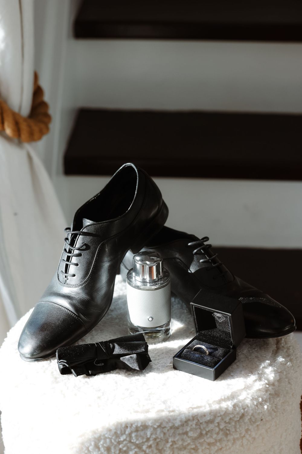 Black dress shoes with bow tie and silver accessories arranged on white surface.